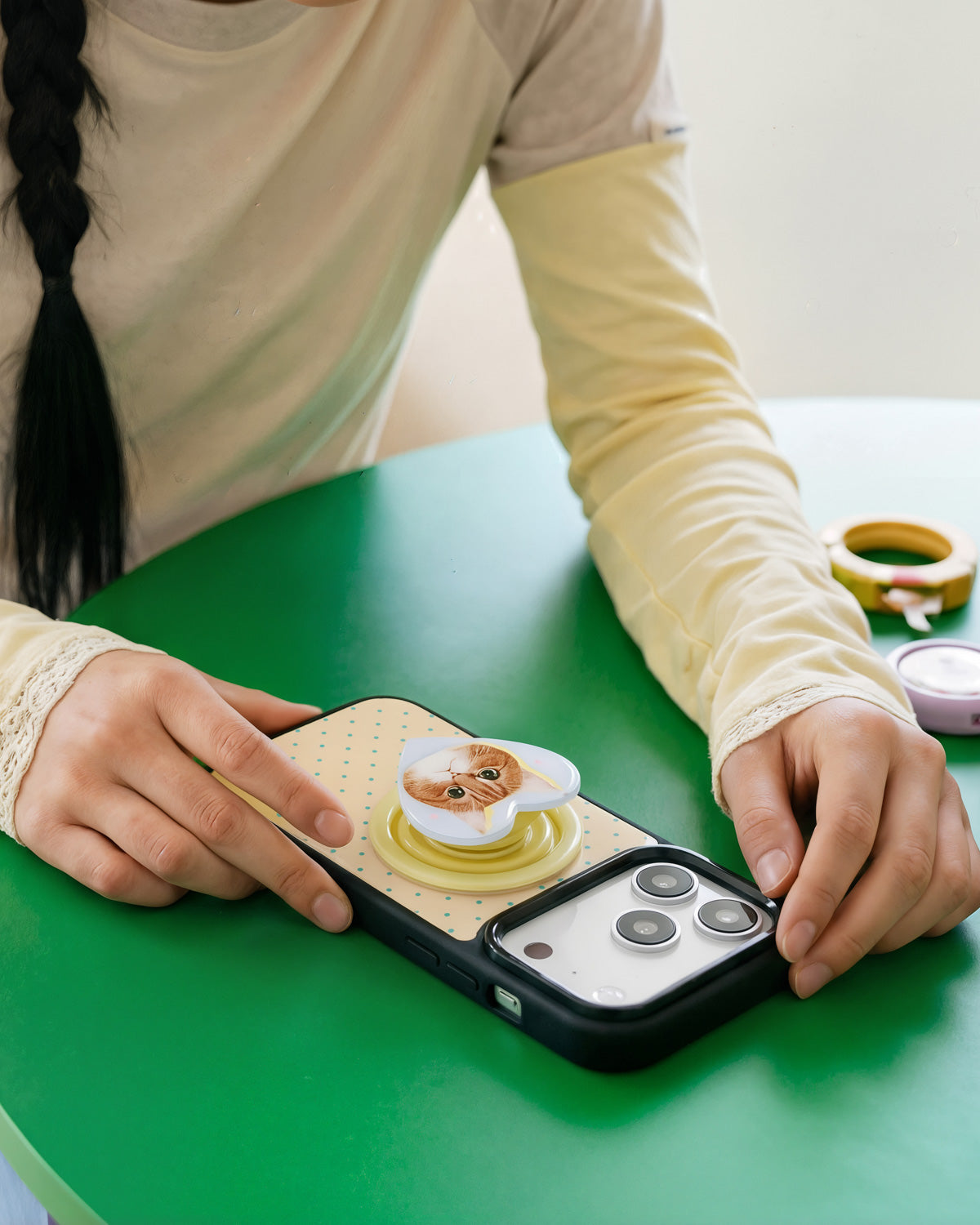 Phone laid flat with the heart-shaped MagSafe grip extended as a kickstand on a green tabletop