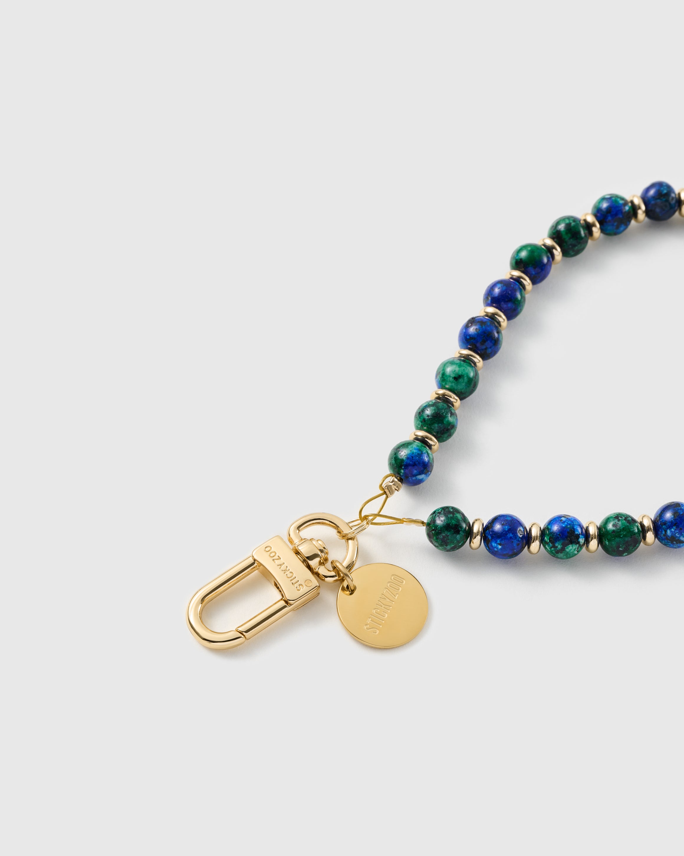 Close-up of the 18K gold-plated hook, engraved STICKYZOO disc and blue-and-green stone beads — each one unique