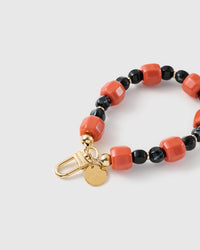 Close-up of the 18K gold-plated hook, engraved STICKYZOO disc and ember-orange and black marbled beads — no two alike