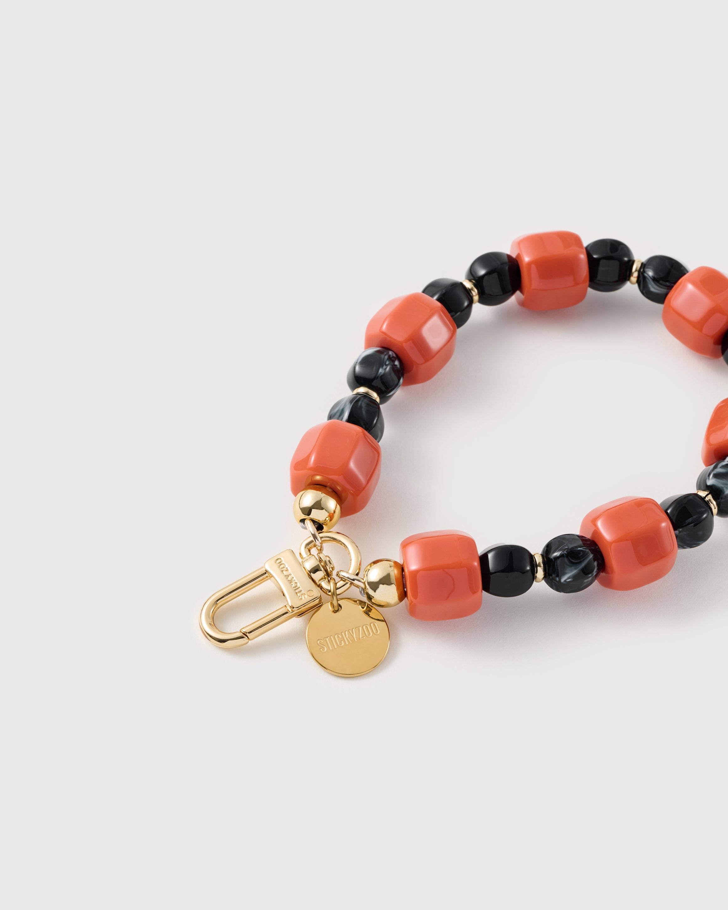 Close-up of the 18K gold-plated hook, engraved STICKYZOO disc and ember-orange and black marbled beads — no two alike