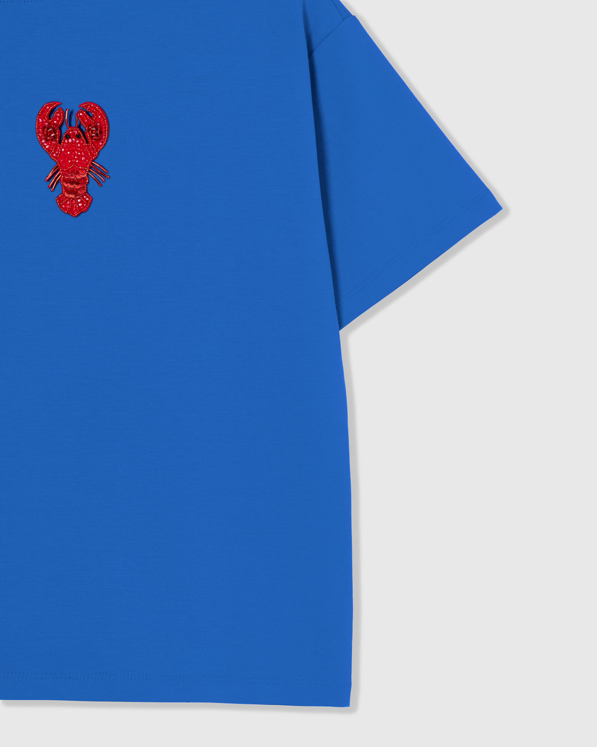 Styled layflat of the blue STICKYZOO Lobster T-Shirt showing the beaded lobster applique and the relaxed dropped-shoulder drape.