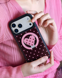 Phone propped between fingers with the pink heart ring kickstand visible on the burgundy case back