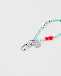 Close-up of silver-tone carabiner clasp and engraved STICKYZOO charm disc with mint beads and red heart