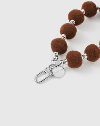 Brown plush phone strap hanging from phone showing hands-free wrist carry