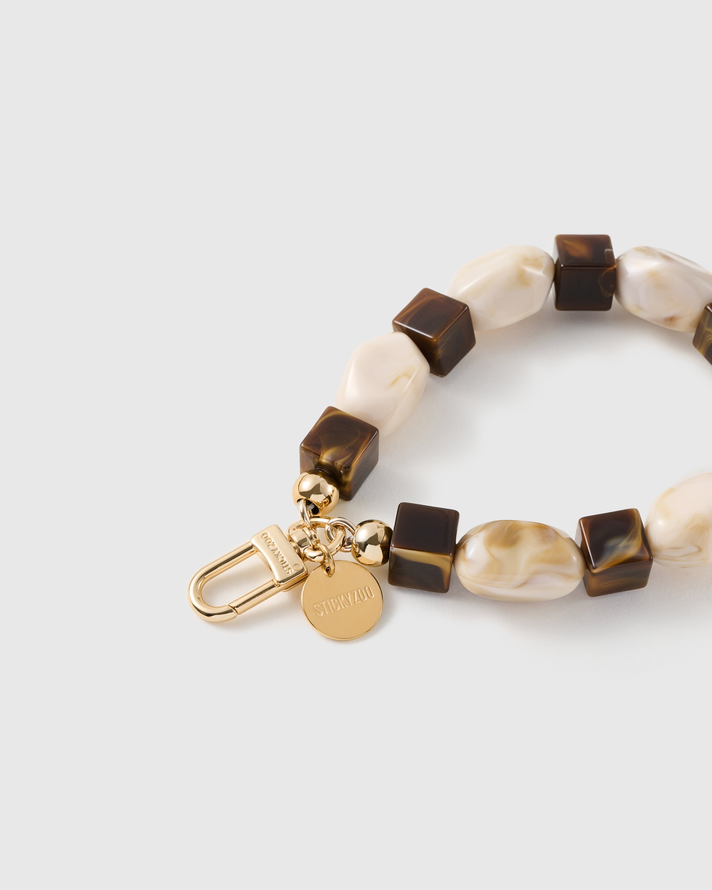 Close-up of the 18K gold-plated hook, engraved STICKYZOO disc and cocoa marbled beads — no two alike
