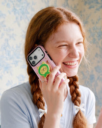 Pink green-hood cat phone case held to the ear during a call with the pop-grip resting against the hand.