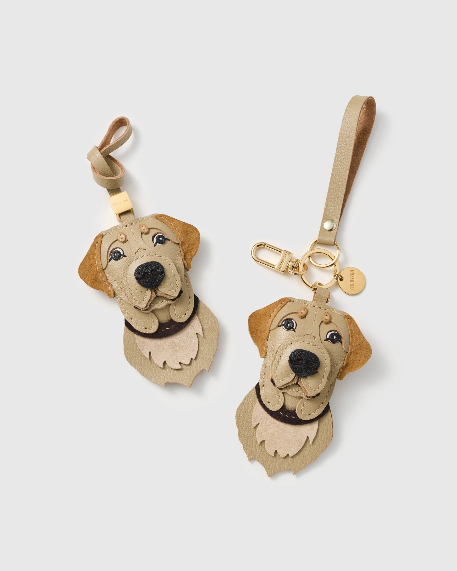 {{Dual attachment.}} Both editions of the Labrador Retriever charm — leather strap loop for bags, or 18K gold-plated keychain clip with engraved disc.