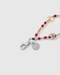 Close-up of silver-tone clasp and engraved charm disc with faceted crimson and peach beads