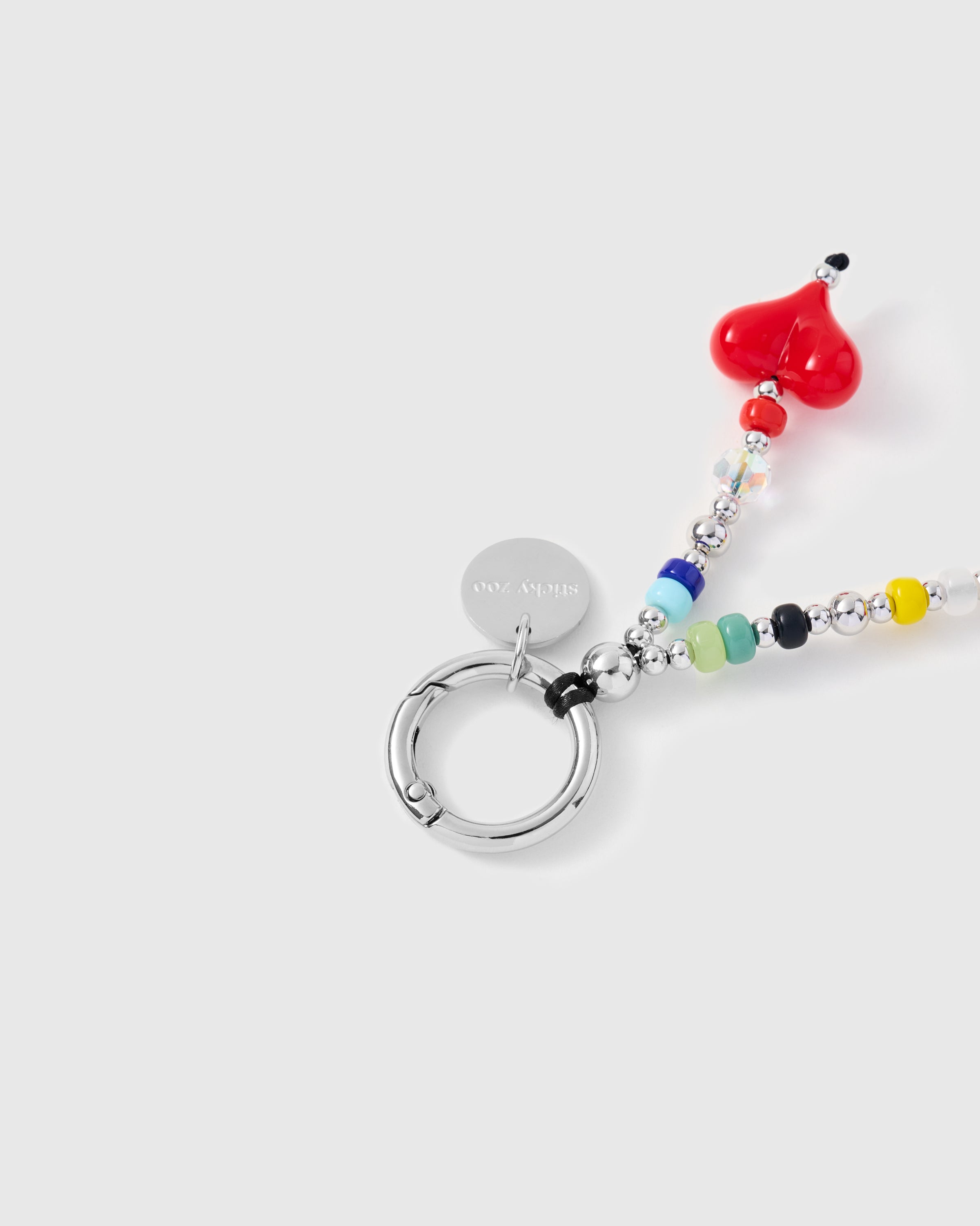 Close-up of silver-tone spring ring and engraved charm disc with red heart and rainbow beads