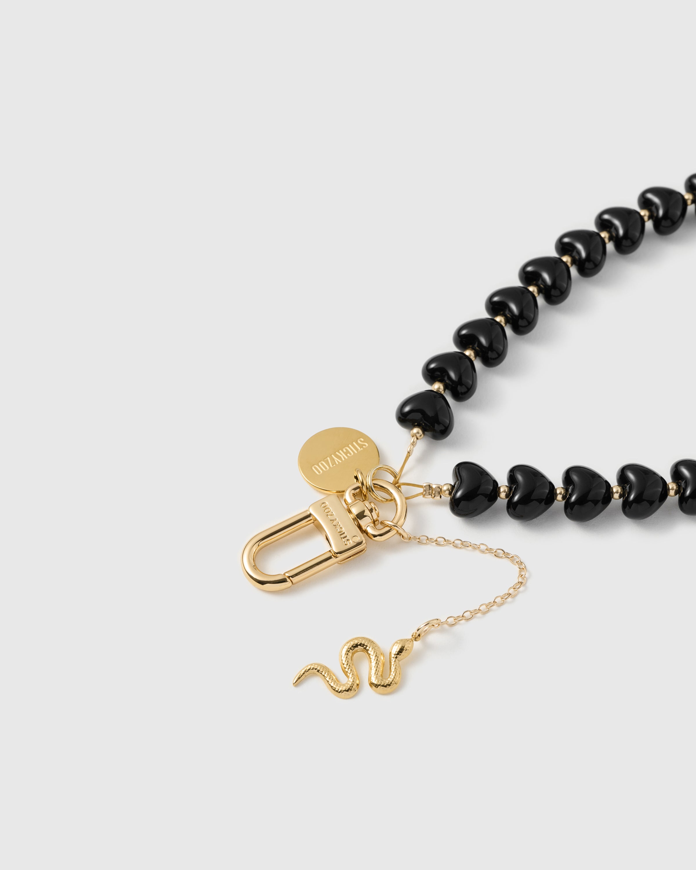 Best Seller close-up of engraved STICKYZOO gold-plated carabiner with noir heart beads and slim gold snake charm in detail