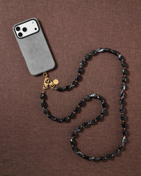 Lifestyle flat-lay of the handmade STICKYZOO NOIR ORBIT cross-body strap resting on fabric