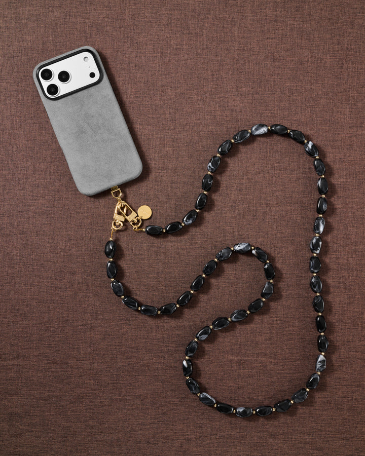 Lifestyle flat-lay of the handmade STICKYZOO NOIR ORBIT cross-body strap resting on fabric