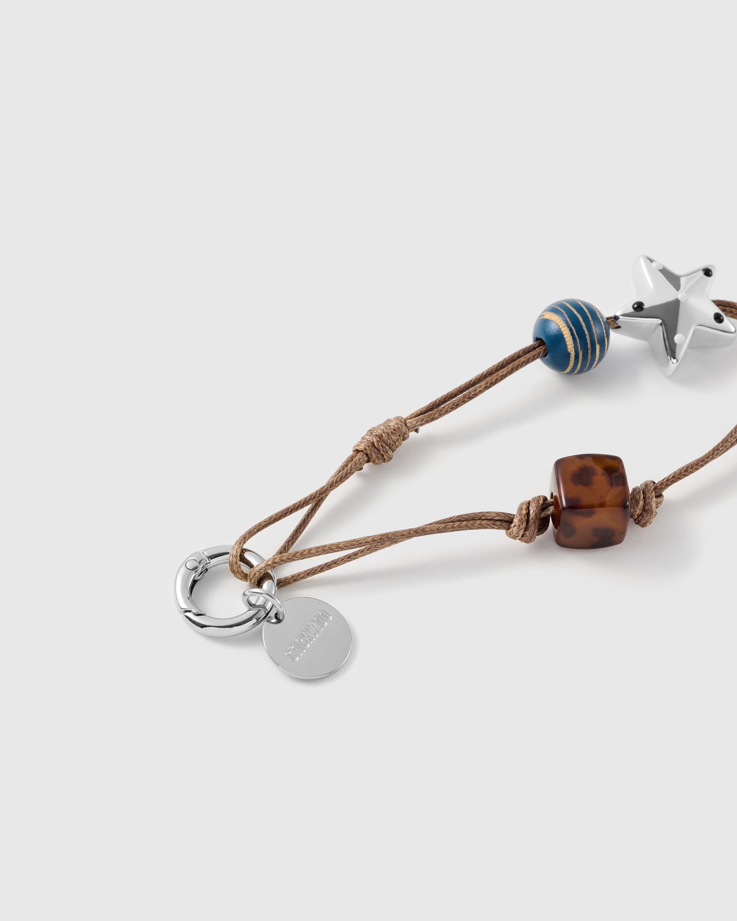 Close-up of the silver-tone star charm, gold-striped blue bead and mottled tortoiseshell cube on knotted tan cord.