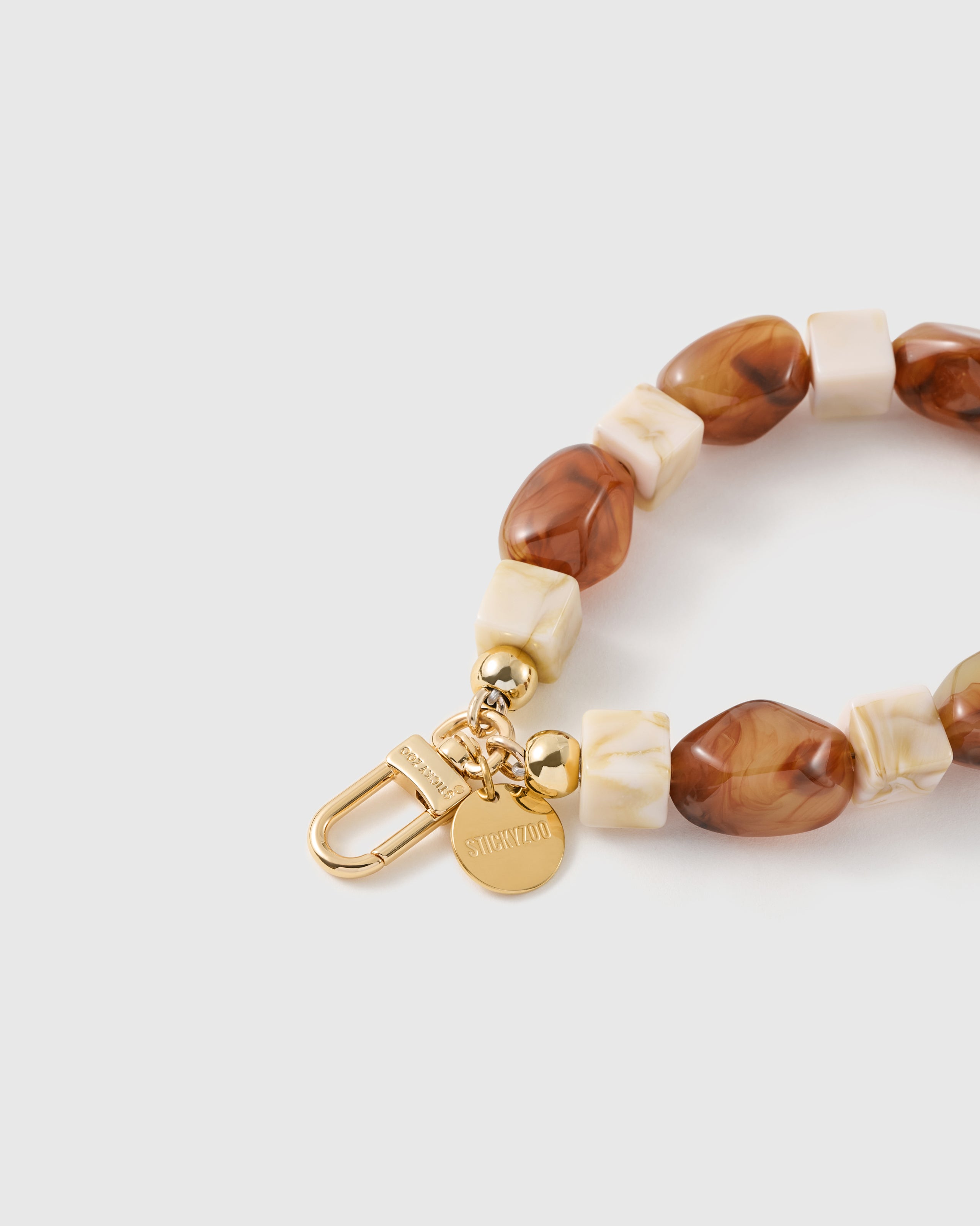 Close-up of the 18K gold-plated hook, engraved STICKYZOO disc and cognac marbled beads — no two swirls alike