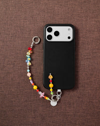 Phone with rainbow crystal bead strap on dark brown textured fabric lifestyle flat-lay
