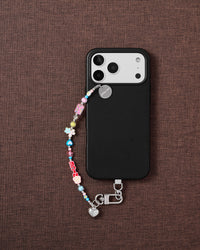Phone with colorful charm bead strap on dark fabric lifestyle flat-lay