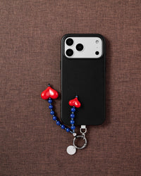 Blue stone and red heart phone charm styled with phone on brown fabric flat-lay