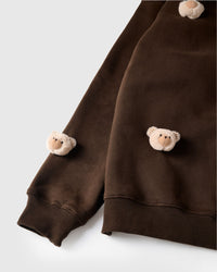 Close-up of plush bear faces at sleeve cuff and lower hem on dark brown cotton