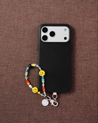 Phone with yellow smiley bead strap on dark brown textured fabric lifestyle flat-lay