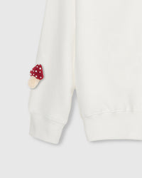 Close-up of hand-stitched mushroom on sleeve cuff showing stuffed texture against cream fabric