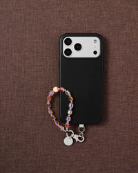 Phone with peach crystal bead strap on dark brown fabric lifestyle flat-lay