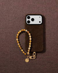 Flat-lay of the handmade stone bead phone strap on soft fabric, showing warm honey, amber and gold tones