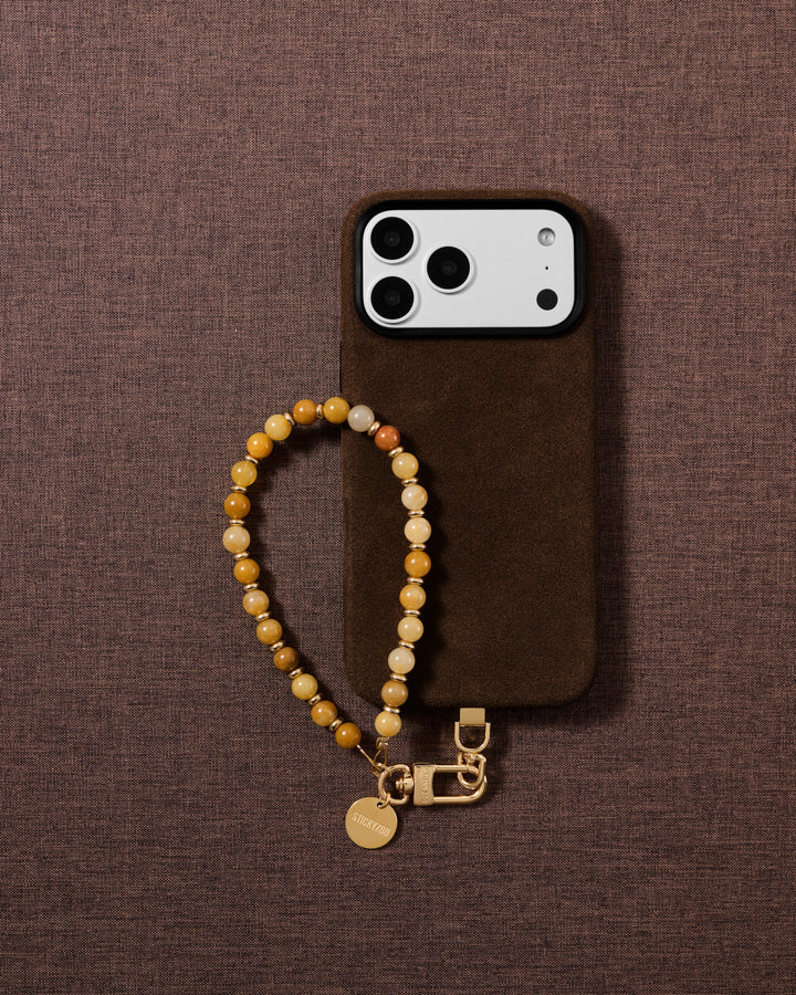 Flat-lay of the handmade stone bead phone strap on soft fabric, showing warm honey, amber and gold tones