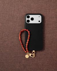 Phone with scarlet stone bead strap on dark brown fabric lifestyle flat-lay