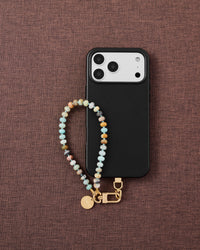 Phone with aqua agate stone strap on dark brown fabric lifestyle flat-lay