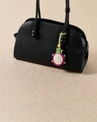 Handmade French Alran pitaya leather charm styled on a black handbag against a tan linen background — summer fruit-as-jewelry detail