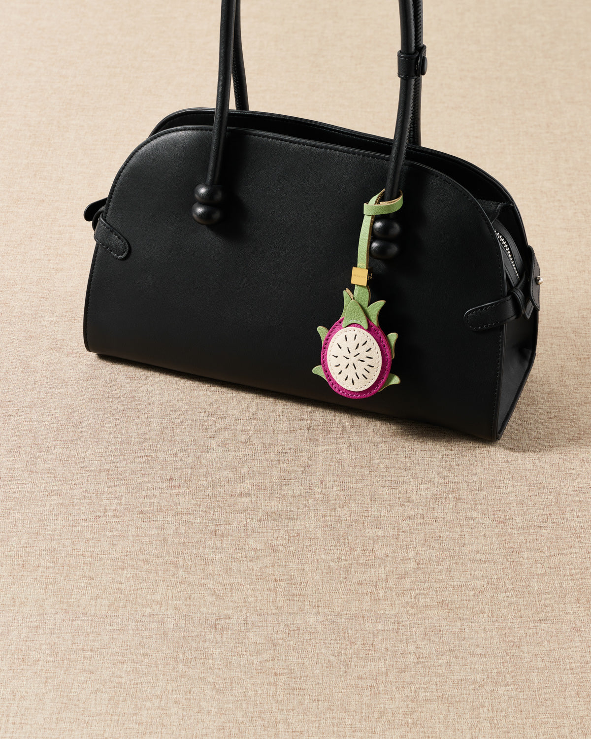 Handmade French Alran pitaya leather charm styled on a black handbag against a tan linen background — summer fruit-as-jewelry detail