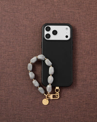Phone with grey marble stone strap on dark brown fabric lifestyle flat-lay