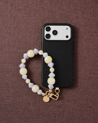 Phone with butter frost cluster strap on dark brown fabric lifestyle flat-lay