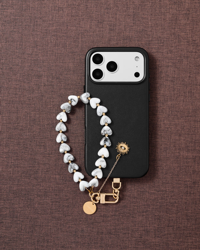 Flat-lay of storm eye amulet phone strap with engraved gold hardware and Phone Strap Card