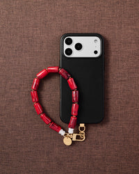 Phone with ruby marble barrel bead strap on dark brown fabric lifestyle flat-lay