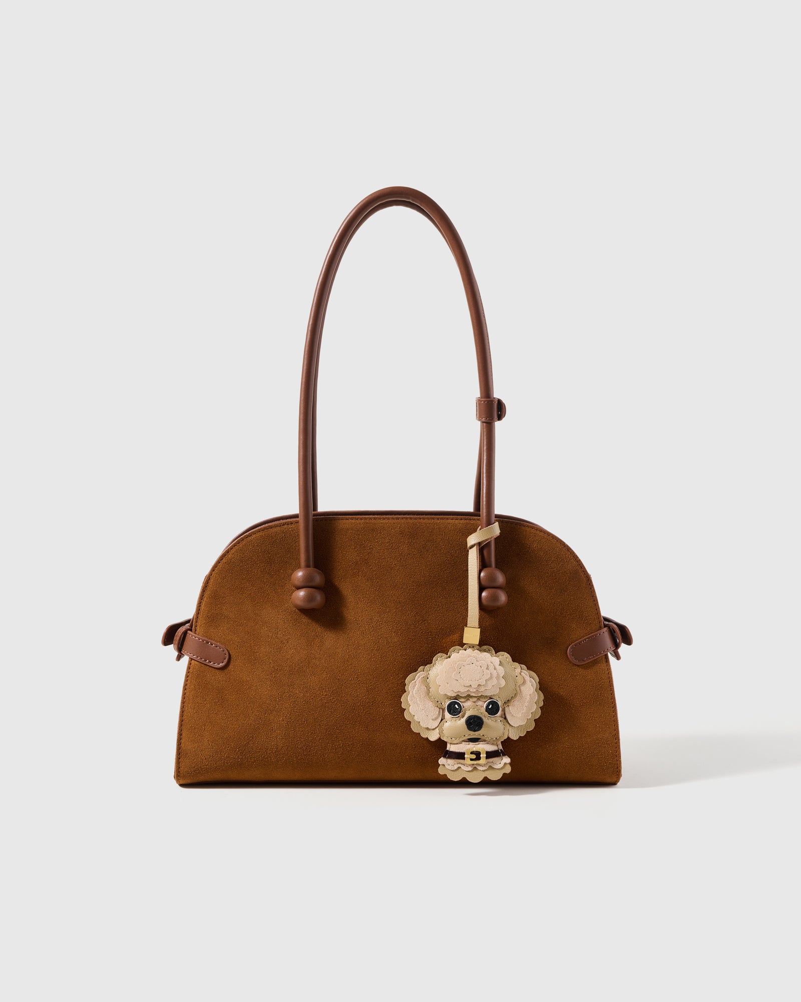 {{A detail people notice.}} on bag — champagne cream against warm brown. French Alran goatskin and alcantara suede. Designed in Amsterdam.