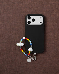 Cloud rainbow beaded phone strap with black phone on dark brown fabric lifestyle flat-lay