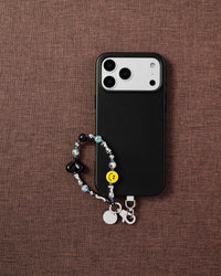 Smiley black heart phone strap flat-lay on dark brown fabric by STICKYZOO