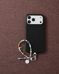 Colorful glass bead phone strap styled with phone on brown fabric lifestyle flat-lay