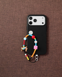 Clown dog beaded phone strap with black phone on dark brown fabric lifestyle flat-lay
