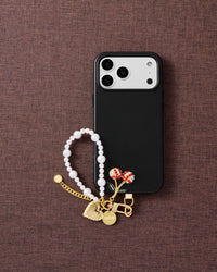 Phone with pearl orbit strap on dark brown fabric lifestyle flat-lay