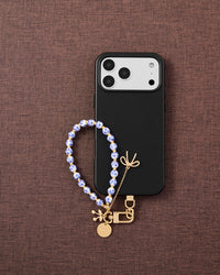 Phone with porcelain bloom charm strap on dark brown fabric lifestyle flat-lay