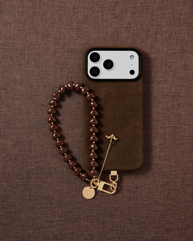 Cocoa Dachshund Heart phone strap and black phone case styled on warm cocoa fabric — daily wrist carry.