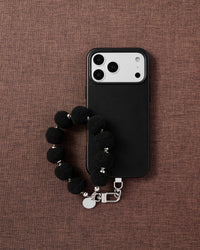 Phone with black pom-pom strap on styled background by STICKYZOO