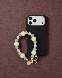 Phone with butter jade mix strap on dark brown fabric lifestyle flat-lay