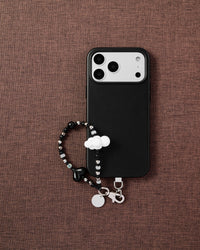 Phone with monochrome heart and cloud bead strap on dark brown fabric lifestyle flat-lay