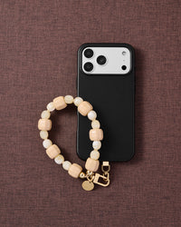 Apricot butter mix phone strap with phone on dark brown fabric lifestyle flat-lay