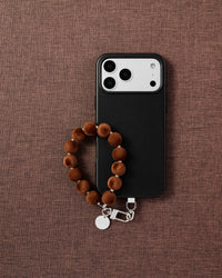 Phone with camel velvet pom bead strap on dark brown fabric lifestyle flat-lay
