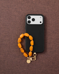 Amber agate phone strap with black phone case on dark fabric lifestyle flat-lay