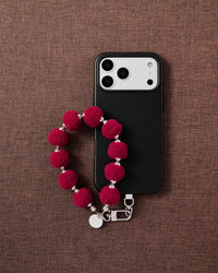 Phone with crimson pom-pom strap on styled background by STICKYZOO